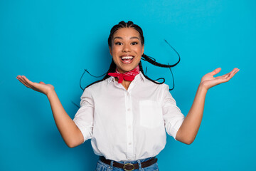 Charming young woman with joyful expression wearing casual outfit and red scarf against bright blue...