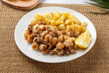 Fried calamari rings with potatoes and lemon slice on white plate