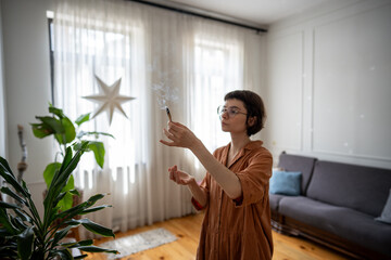 Focused woman do personal ceremony with smudging stick to refresh and enhance mental clarity....