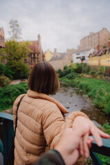 Woman in down jacket clothes leading man to the dean village in edinburgh, Scotland. Traveling together. Follow me.