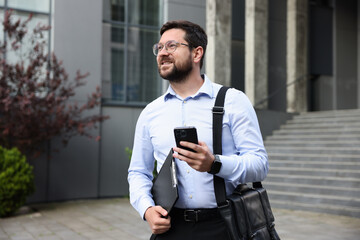 Successful businessman with smartphone near office building