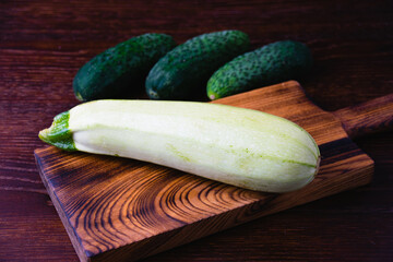 Zucchini and cucumbers on a cutting board, on a dark wooden background. Concept of healthy cooking...