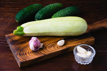 Cucumbers, garlic and zucchini on a cutting board, on a dark wooden background. Concept of cooking...