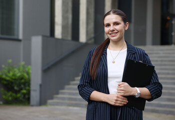 Happy businesswoman with folder near office building. Space for text
