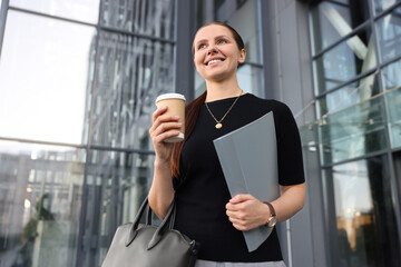 Successful businesswoman with coffee and folder near office building, low angle view