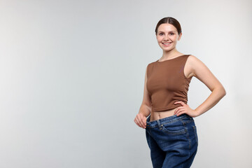 Beautiful woman wearing old jeans after weight loss on light grey background, space for text