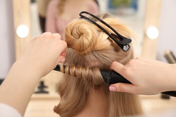Fototapeta premium Hairdresser curling woman's hair in salon, closeup