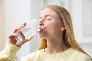 Young woman drinking water from glass at home