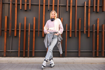 Beautiful young woman with roller skates near building outdoors
