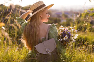 Woman with beautiful wildflowers, hat and backpack in meadow on sunny day, back view
