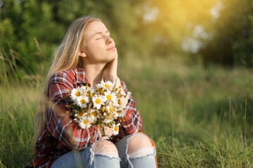 Beautiful woman with wildflowers enjoying summer day in meadow. Space for text