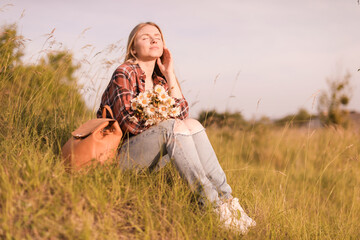 Beautiful woman with wildflowers and backpack enjoying summer day in meadow. Space for text