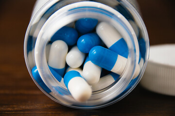 White and blue pills in a jar, macro on a dark wooden background. Self-medication concept.