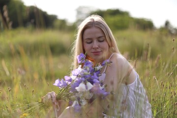 Beautiful woman with bouquet of wildflowers enjoying sunny day in meadow