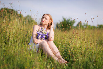 Beautiful woman with bouquet of wildflowers enjoying sunny day in meadow