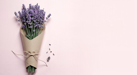 Bouquet with lavender elegantly wrapped in craft paper and tied, isolated on pink background with copy space.