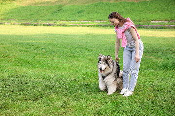 Smiling woman with her cute Alaskan malamute dog on green grass outdoors. Space for text