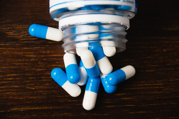 White and blue pills in a jar, macro on a dark wooden background. Self-medication concept.