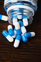 White and blue pills in a jar, macro on a dark wooden background. Self-medication concept.