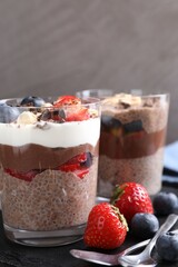 Delicious chocolate puddings with chia seeds, nuts and berries in glasses on table, closeup