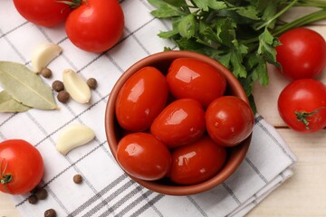 Tasty pickled tomatoes in bowl and ingredients on light wooden table, flat lay