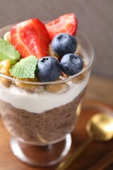 Delicious chocolate pudding with chia seeds, nuts and berries in glass on wooden table, closeup