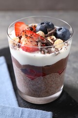 Delicious chocolate pudding with chia seeds, nuts and berries in glass on grey table, closeup