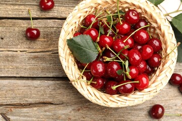 Fresh wet cherries and leaf in wicker basket on wooden table, flat lay