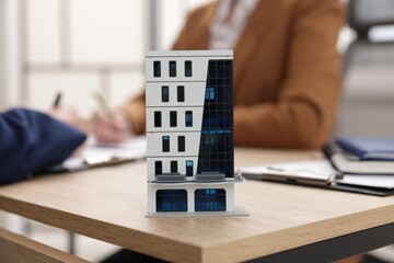 Real estate agent working with client at desk in office, focus on house model