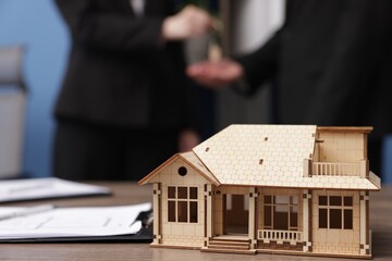 Real estate agent giving key to client in office, focus on house model on desk