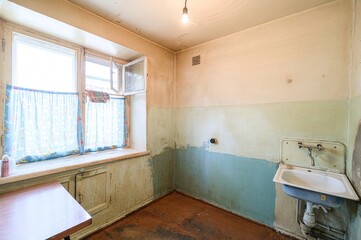 worn kitchen with peeling paint, an old sink, and a window with floral curtains. The room feels dated and shows signs of wear and tear