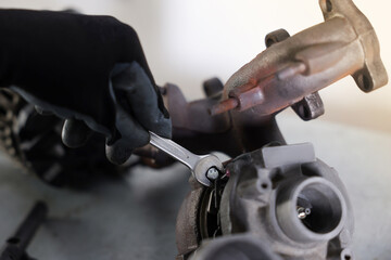 Auto parts. Professional mechanic with wrench fixing turbocharger at grey table indoors, closeup