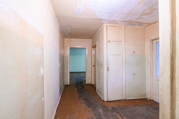 interior shot of a worn hallway. The walls show signs of damage, and the floor is stained. Several...