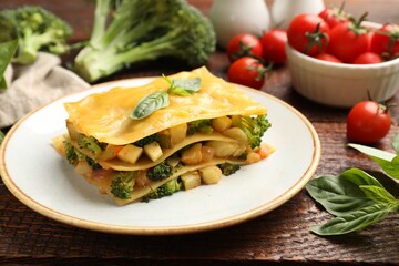 Piece of tasty vegetarian lasagna and ingredients on wooden table, closeup