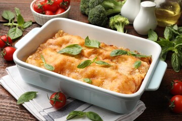 Tasty vegetarian lasagna in baking dish and ingredients on wooden table, closeup