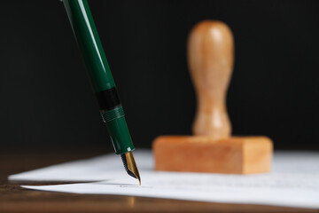 Signing notary document with fountain pen at table against black background, closeup