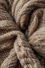 A close-up of light brown knitted fabric, showcasing distinct braided textures and soft, warm tones. Ideal as a cozy background, for textile designs, or winter and comfort themes.