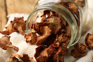 Dried chanterelle mushrooms in jar and towel on wooden table, closeup