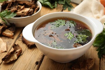 Tasty soup with mushrooms and parsley in bowl on wooden table, closeup