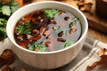 Tasty soup with mushrooms and parsley in bowl on table, closeup