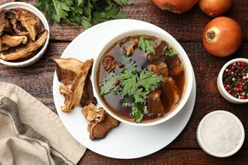 Tasty soup with mushrooms and parsley in bowl on wooden table, flat lay