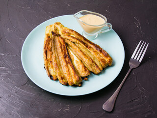 Delicious fried zucchini with aromatic sour cream garlic sauce on a plate on dark table