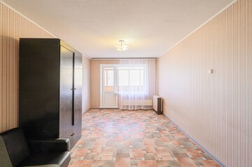 interior view of a room with striped wallpaper, tile flooring, a dark wardrobe, sofa, and a door leading to a balcony. Natural light fills the space