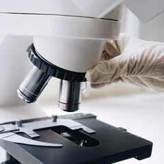 Close-up of a gloved hand adjusting the objective lenses of a compound microscope, highlighting...