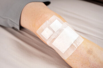 Close-up of an injured male knee covered with adhesive bandages, patch, resting on a light surface....