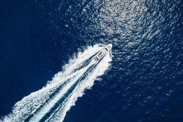 Fototapeta na wymiar High aerial top view of a luxury yacht cruising with high speed over blue ocean leaving a trail of bubbles and waves behind