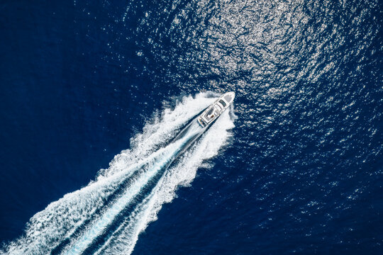 High aerial top view of a luxury yacht cruising with high speed over blue ocean leaving a trail of bubbles and waves behind