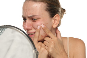 Studio shot of young woman with acne squeezing pimples in pain, isolated on white background