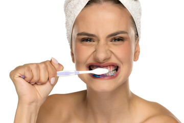 Young woman fiercely brushing teeth with blue toothpaste, studio shot on white background.