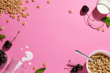 Grain rings, cherries, mint leaves, a spoon, spilled milk, and a bowl on pink background. A breakfast concept with space for your text.